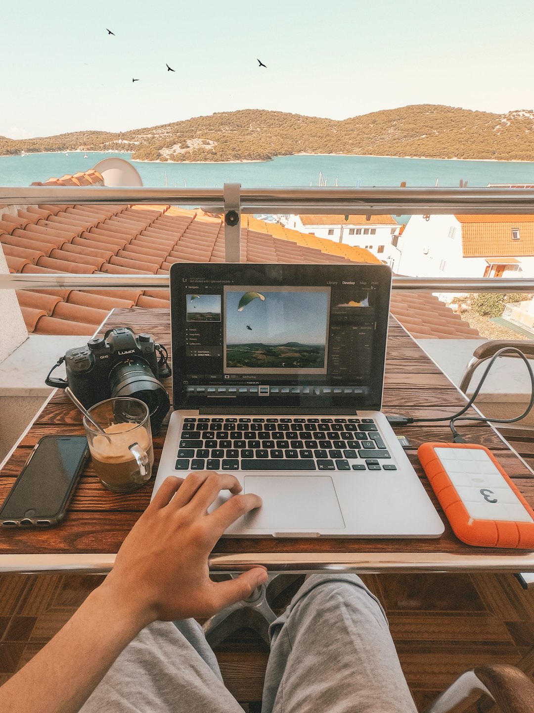 Person edits photos on laptop on sunny balcony with ocean view.
