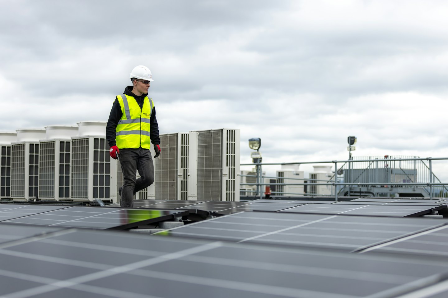 Technician inspects solar panels and HVAC units on a commercial rooftop.